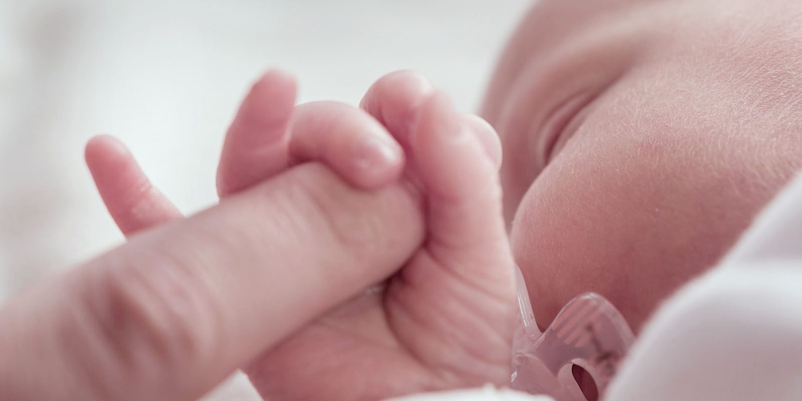 close-up of a newborn baby with its fingers wrapped around the finger of an adult