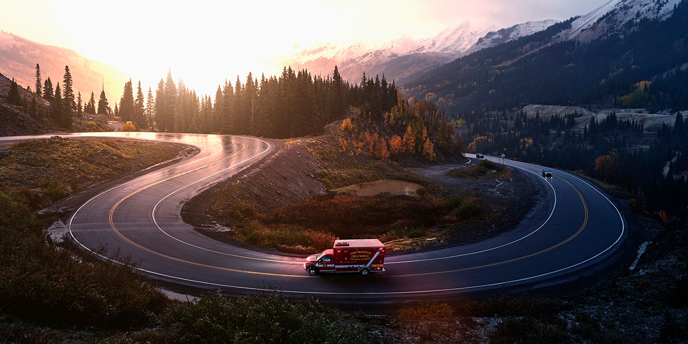 a Medix ambulance drives around a curved road in the mountains in early morning