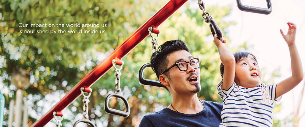 a father with glasses helps his young son swing from handles from an overhead bar on a playground