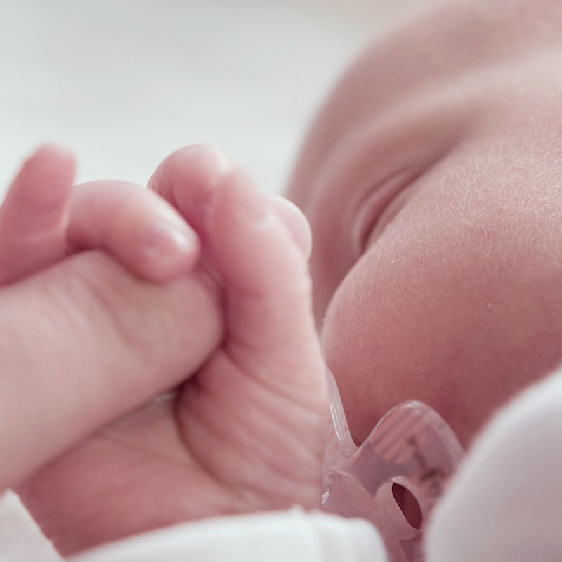 close-up of a newborn baby with its fingers wrapped around the finger of an adult