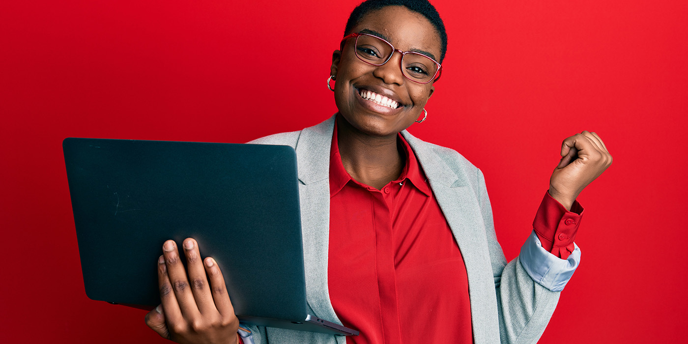 happy woman with glasses wearing red shirt and holding a laptop in one hand